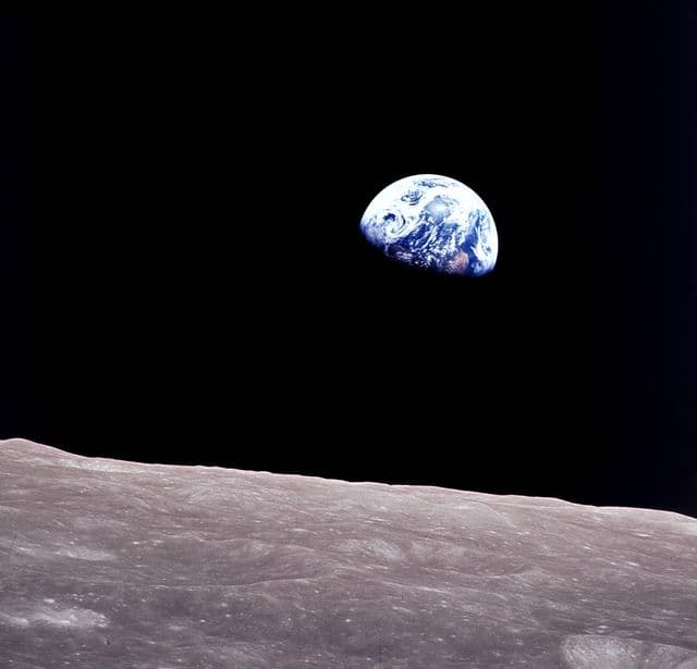 A blue-and-white Earth rises above a gray, cratered lunar horizon, suspended in black space.
